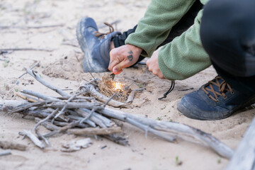 Bushcraft expert starting campfire with fire starter on sand