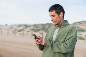 Obraz premium Young man texting on smartphone at sandy beach