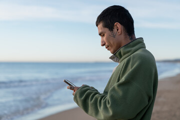 Young man using smartphone on beach connecting online © Cavan