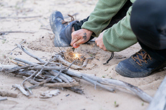 Bushcraft expert starting campfire with fire starter on sand