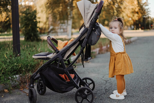 Toddler in yellow dress standing with a stroller outside.
