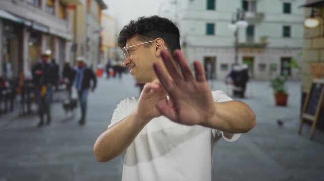 Man pushes forward his hands in a stop gesture and grimaces adjusting his glasses on a crowded urban street; rejection.