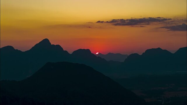 Golden hour time lapse showing sun setting behind mountains, capturing vibrant orange glow of the sky and silhouette of the peaks