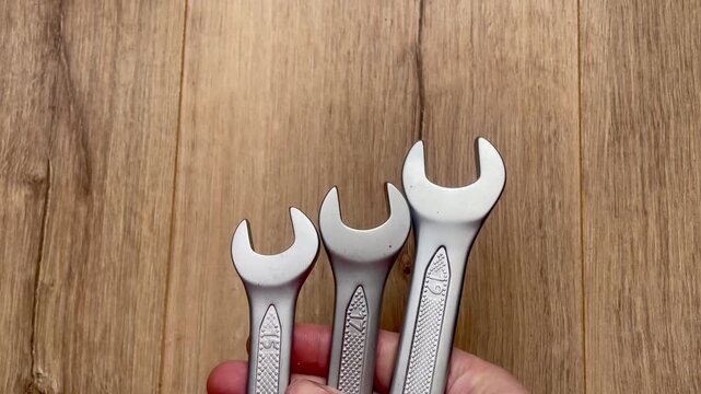 Hand holding three silver open end wrenches against wooden background