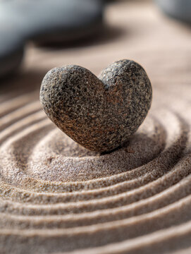 Heart-shaped stone placed on raked sand creating serene circular patterns symbolizing balance and tranquility in a minimalist zen garden setting