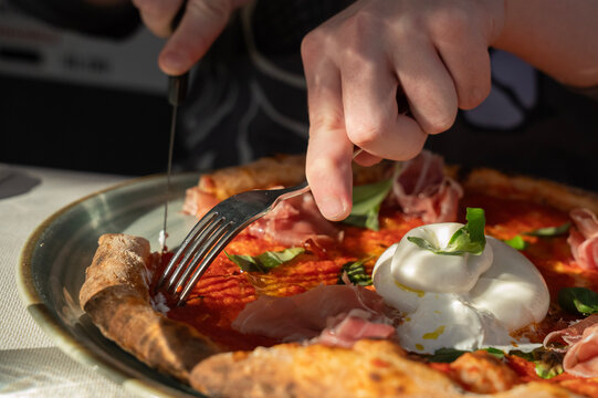 dłonie osoby krojącej kawałek pizzy
