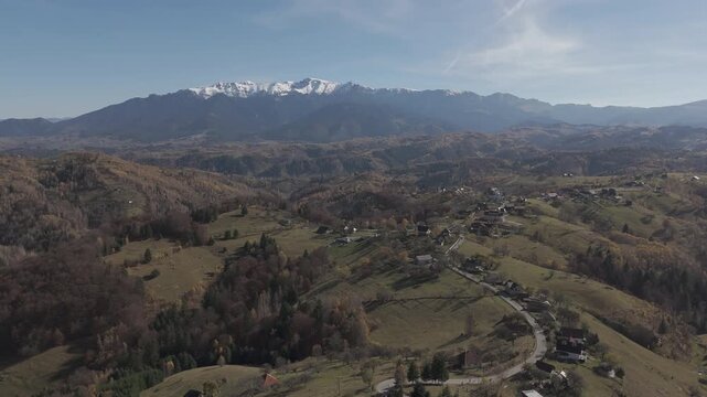 Breathtaking Autumn Village and Hillcrest Road in Pestera under Snow Capped Bucegi Mountains Aerial Descending Shot 4K Ungraded Log