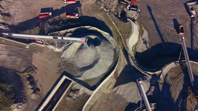 Heavy machinery operates efficiently at a construction site on a clear day. Trucks transport gravel while conveyor belts distribute materials across the site, illustrating diligent work dynamics.