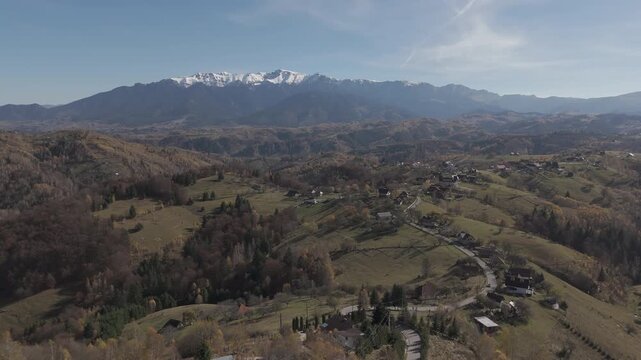 Picturesque Autumn Hillcrest Village and Driving Cars in Pestera under Snow Capped Bucegi Mountains Aerial Descending Shot 4K Ungraded Log