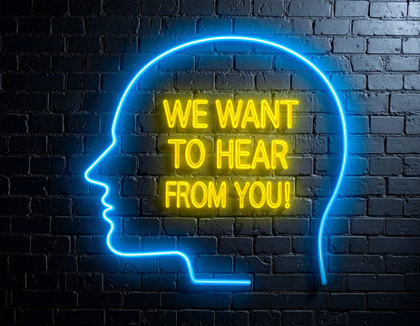 Leuchtende gelbe Neonschrift "we want to hear from you!" umramt von einem blauen Neongesicht auf dunkler Backsteinmauer