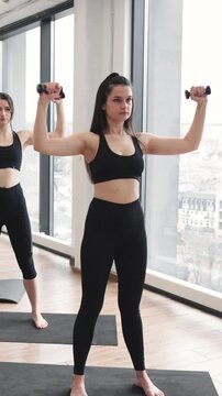 A woman in athletic wear performs a dumbbell exercise, focusing on her arm strength and muscle definition during a fitness class
