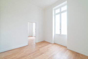 Bright empty room in a renovated apartment with white walls, wooden floor and large window. Minimalist interior space ready for furnishing or moving in.