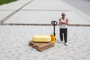 Miniature worker stands beside pallet jack holding yellow cargo © yl