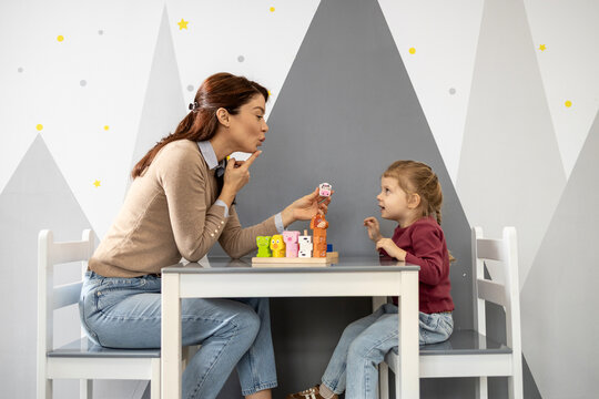 Speech therapist guiding a young girl through playful oral-motor exercises with educational toys during a focused private session to improve pronunciation and communication skills