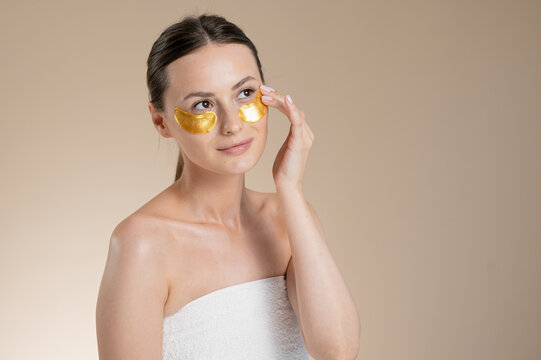 Woman applying golden under eye patches for skincare and rejuvenation