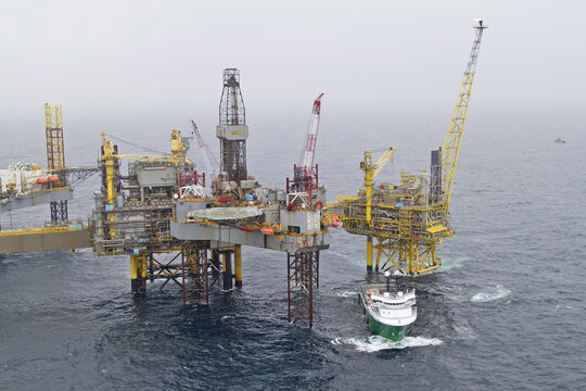 Esbjerg, Denmark - 13 February 2026: Aerial view of a colossal offshore oil rig standing defiantly against the grey sea, a vessel navigating the choppy waters below.