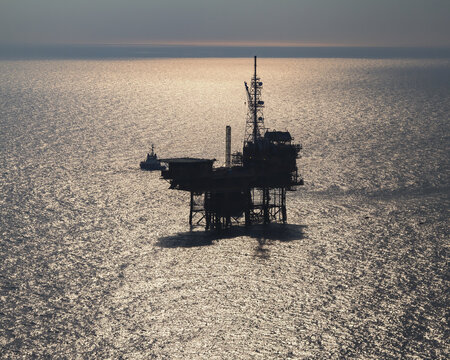 Netherlands, Netherlands - 13 February 2026: Aerial view of a solitary offshore oil rig stands defiant against the shimmering, sun-kissed waters, its silhouette a stark contrast to the serene horizon.