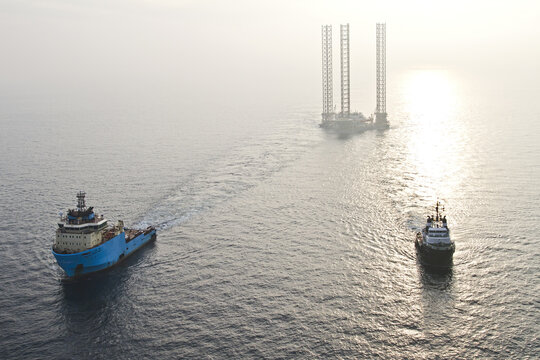 Netherlands, Netherlands - 13 February 2026: Aerial view of the rough sea with a vessel towing a platform, the sun glinting off the waves in the distance.
