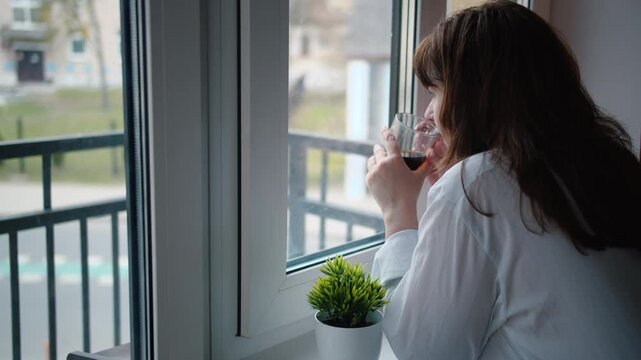Woman's Delightful Coffee Moment by the Window on a Rainy, Overcast Day