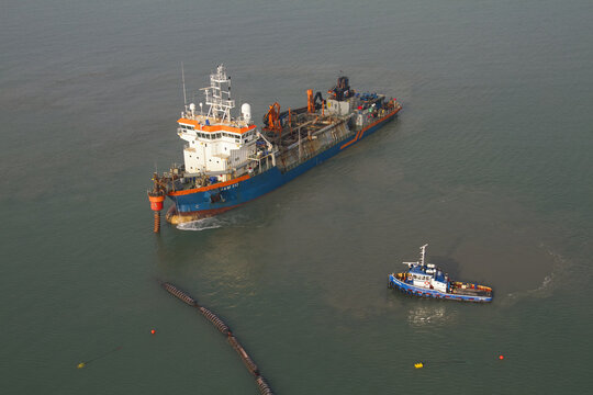 Monster, Netherlands - 13 February 2026: Aerial view of a dredger ship cutting through the tranquil, turquoise sea waters, leaving a trail of sediment in its wake, observed from above.