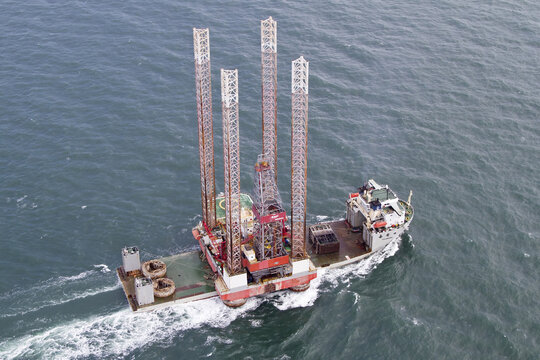 Hoek van Holland, Netherlands - 15 February 2026: Aerial view of a jack-up vessel with a red and white structure cutting through the choppy, dark blue sea, leaving a trail of white foam.