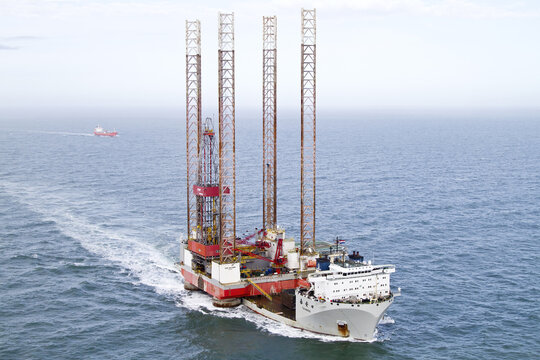 Hoek van Holland, Netherlands - 15 February 2026: Aerial view of a colossal jack-up rig vessel cutting through the deep blue sea, leaving a foamy white trail in its wake.