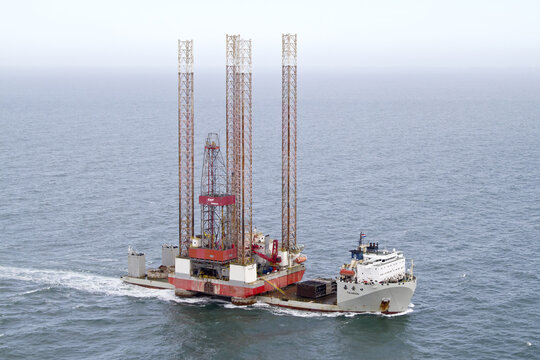 Hoek van Holland, Netherlands - 15 February 2026: Aerial view of a colossal, rust-tinged oil rig platform cutting through the tranquil, silvery sea, contrasting against the sky.