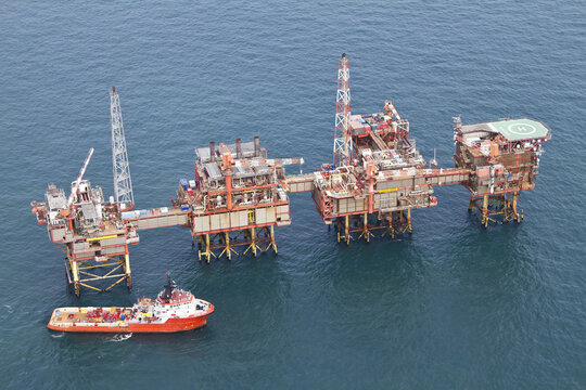United Kingdom, United Kingdom - 15 February 2026: Aerial view of an offshore oil rig platform standing firm against the relentless waves, a stark contrast to the vessel sailing nearby.