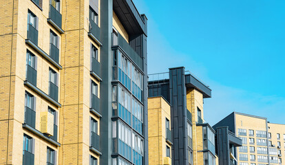 Fototapeta premium Modern apartment buildings against blue sky with brick exterior. Residential architecture featuring balconies and windows. Urban housing concept for real estate, development, city..
