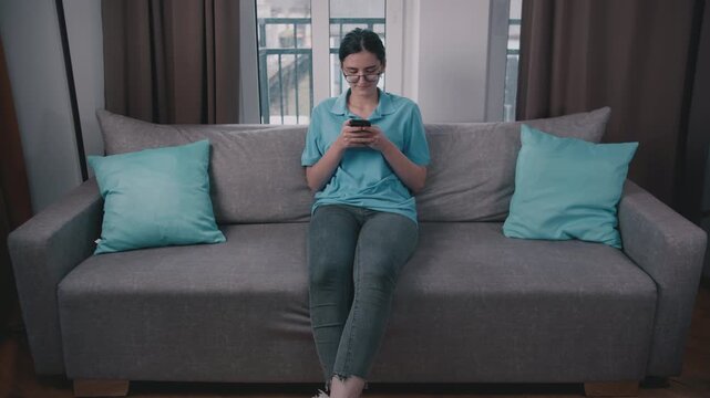 Teenage Girl Sitting on the Couch in the Evening, Engrossed in Texting on Her Phone