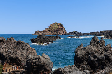 Natural lava pools filled with Atlantic seawater beside basalt formations at Porto Moniz Madeira Portugal, blue water contrasts with black rocks and distant ocean swells beneath open sky