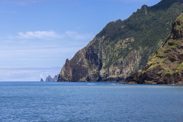 Rocky headland and sea cliffs from Porto da Cruz seafront promenade, Larano Cape rises above calm Atlantic water under blue sky on Madeira Island Portugal
