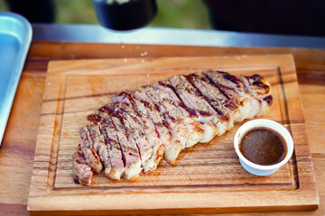 Sizzling Steak Culinary Delight: A mouthwatering, perfectly grilled steak, artfully sliced and presented on a rustic wooden board, accompanied by a small ramekin of rich, savory sauce.