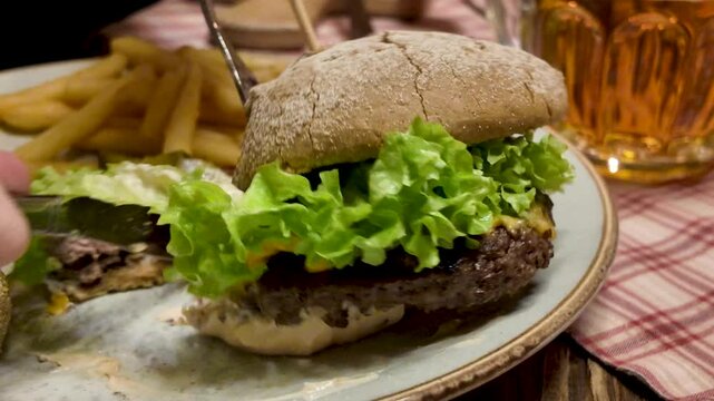 Hamburger being eaten, with knife and fork. Close-up.