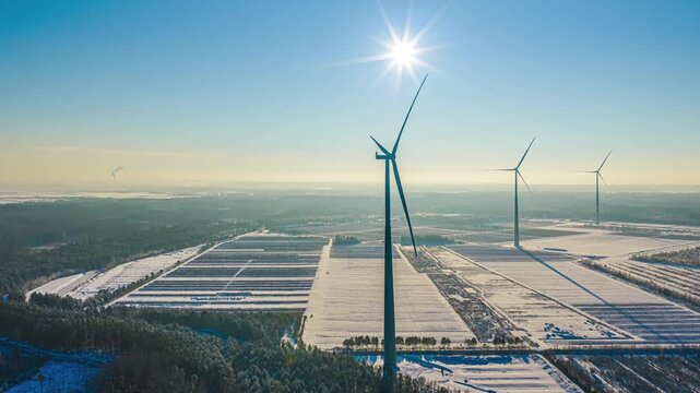 Wind turbines generating clean energy in a winter environment under bright sun in aerial hyperlapse