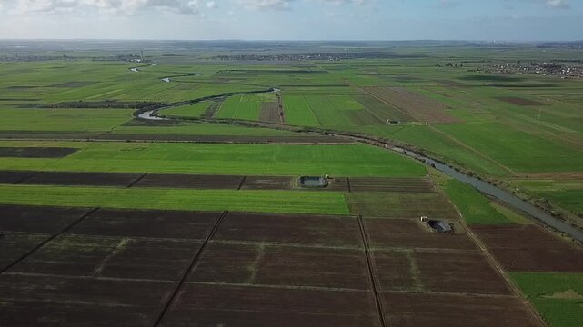 A comprehensive drone view of the Larache agricultural plains. Captures the harmony between natural reed-lined streams, modern irrigation canals, farm reservoirs, and the distant city horizon.