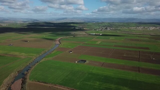 Captivating drone footage showcasing the play of light and shadow over Moroccan farmlands. Features a scenic waterway, traditional rural housing, and the peaceful rolling hills of Larache.