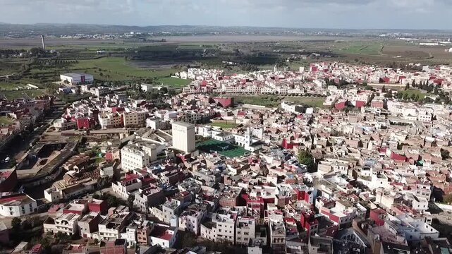 A breathtaking high-angle drone shot capturing the entire urban fabric of Larache. Features the Grand Mosque, traditional neighborhoods, and the vast green farmlands stretching to the horizon.