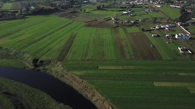 Scenic drone shot overlooking a peaceful rural community in Northern Morocco. Features vast green crop fields, traditional houses, and the beautiful rolling hills of the Larache countryside.