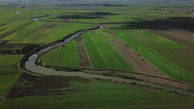 Stunning drone perspective of a winding waterway in Northern Morocco. Captures the fertile agricultural landscape, traditional farming plots, and the distant urban skyline under a clear sky.