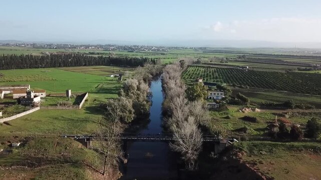 Drone shot of a vital water canal derived from the Loukkos river. Captures the bridge, riverside forest, and its role in supplying water to the vast agricultural plains of Northern Morocco.