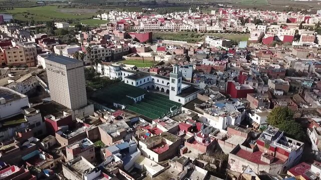 Side-angle drone shot capturing the intricate architecture of Larache's Grand Mosque. Highlights the historic minaret, inner courtyard, and the surrounding traditional Moroccan city dwellings.
