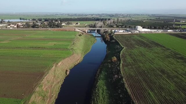 Captivating drone footage featuring a flock of white birds in flight over a Moroccan water canal. Showcases the lush green landscape, rural bridges, and the industrial hub near the river.