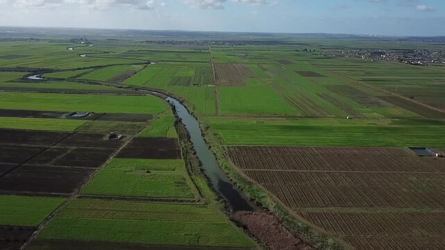 A wide-angle drone view capturing the immense scale of Moroccan agriculture. Features the main irrigation canal flowing through a patchwork of fertile fields under a clear blue sky.