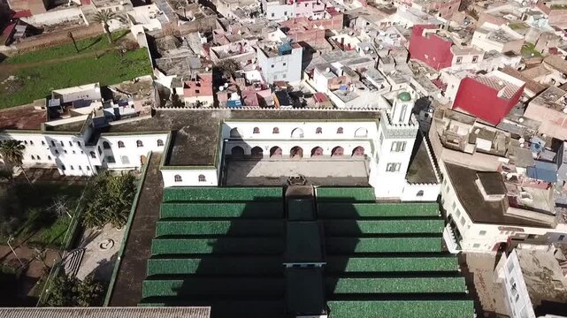 Detailed drone shot capturing the inner architecture of Masjid al-Aazam. Highlights the traditional Moroccan arches, the white minaret, and the symmetrical green roofs in the heart of Larache.