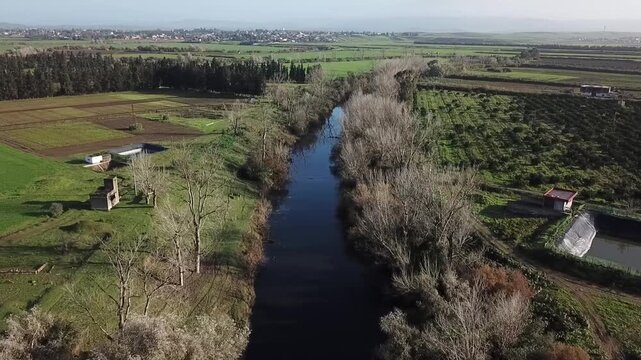 High-definition drone footage of a water canal in Larache. Features riverside forest, traditional agricultural plots, and a scenic view of the countryside leading to the city of Larache.