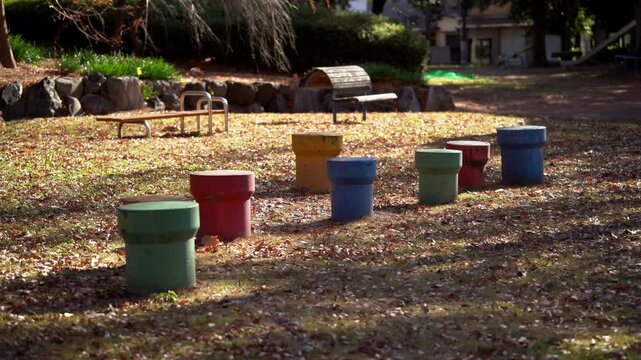 Colorful stepping stools arranged in a sun-dappled park, surrounded by fallen autumn leaves