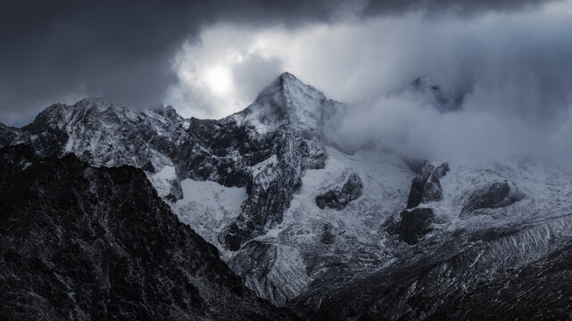 View of snow-capped peaks pierce the swirling mist, their stark white faces contrasting against the brooding sky, creating a scene of sublime drama, Valmalenco.