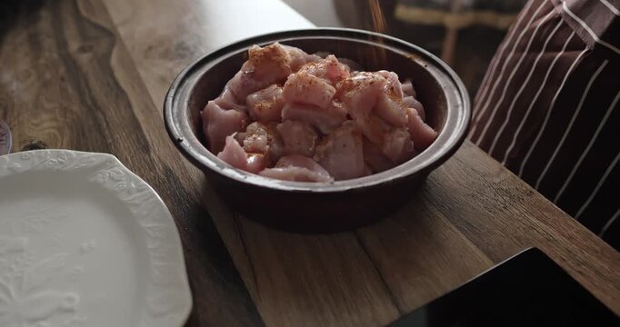 Chef seasoning and mixing raw chopped chicken breast fillet with spices in ceramic bowl on wooden table, preparing healthy protein meal in cozy home kitchen. Healthy food, diet