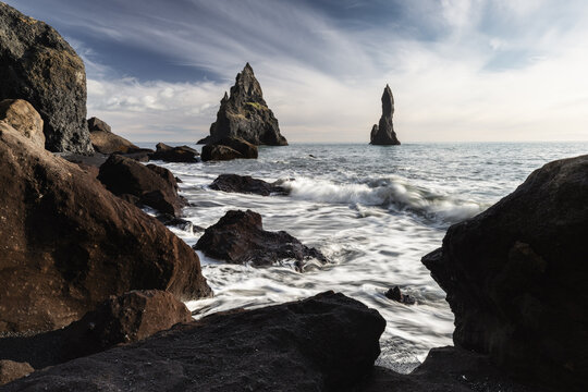 View of jagged basalt sea stacks rise dramatically from the turbulent, white-foaming Atlantic waters off a black sand beach, Reykjav&Atilde;&shy;k, Reykjav&Atilde;&shy;kurborg, Iceland.